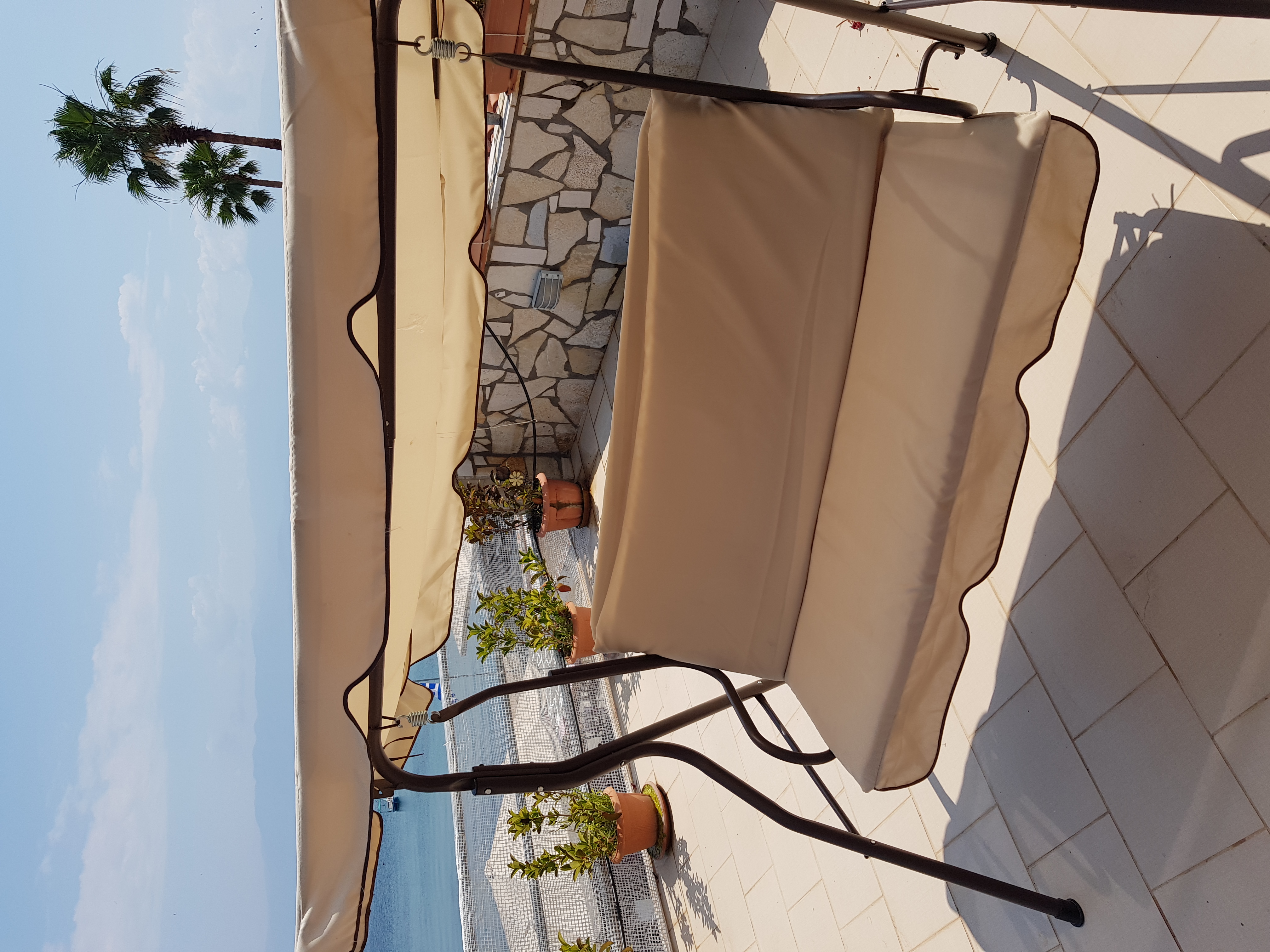 Terrace with swing seat, sea and palm tree in summer